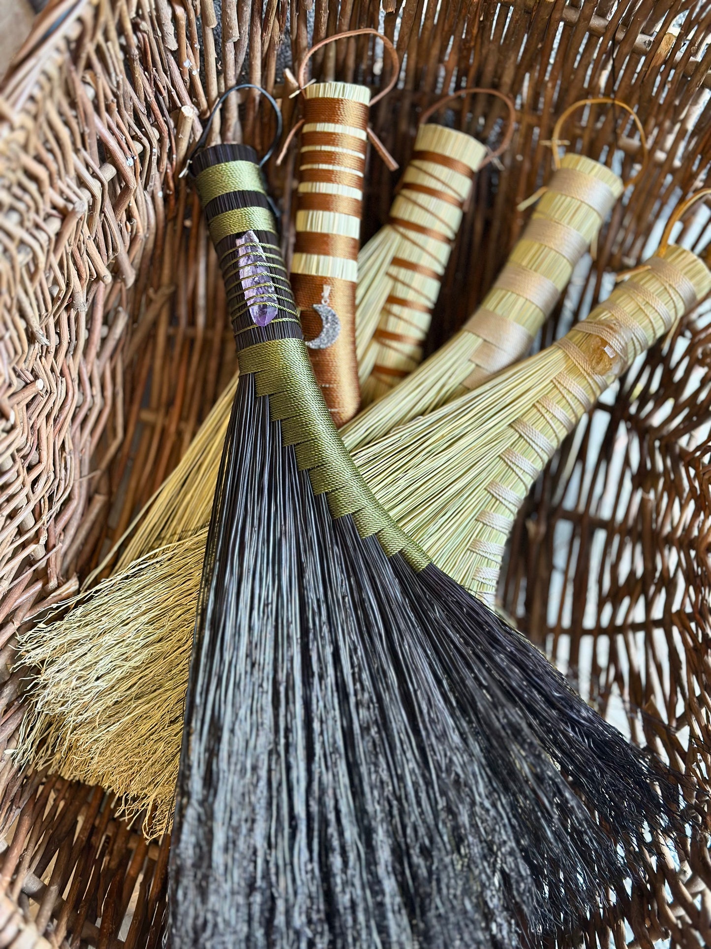 Set of brooms in a basket each of a different design and colour twine some have crystals attached another has a druzy moon pendant attached
