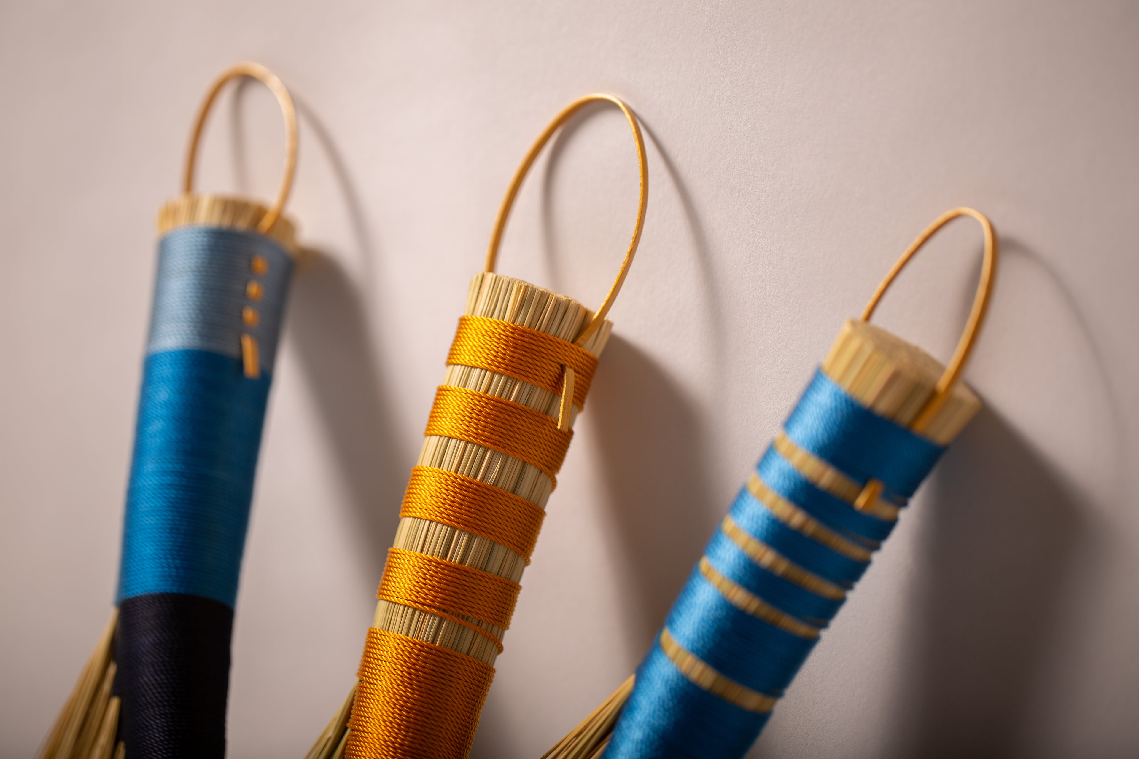 Three hens wings hand brooms in blues and gold twines and natural broomcorn handles closeup