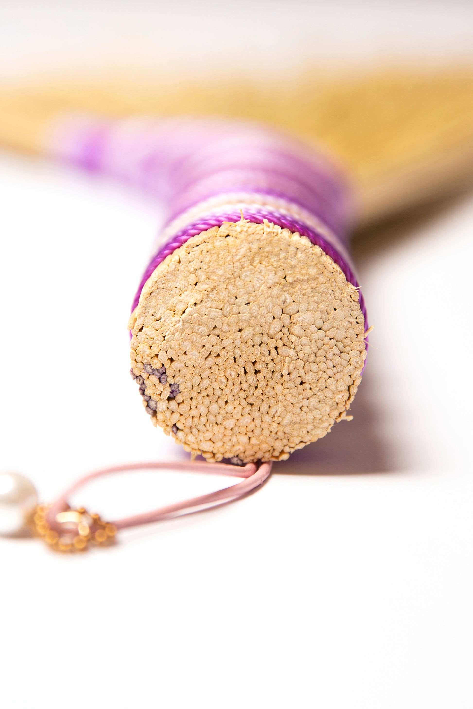 View of a hand broom handle wrapped in purple twine against a white background