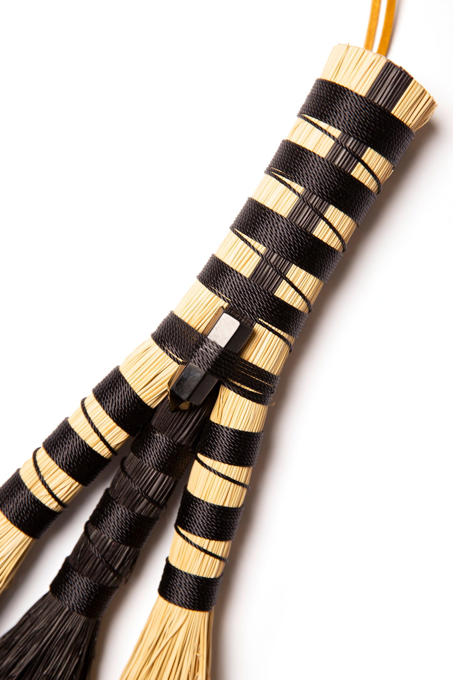 Close up of hand broom with black twine and black tourmaline against a white background
