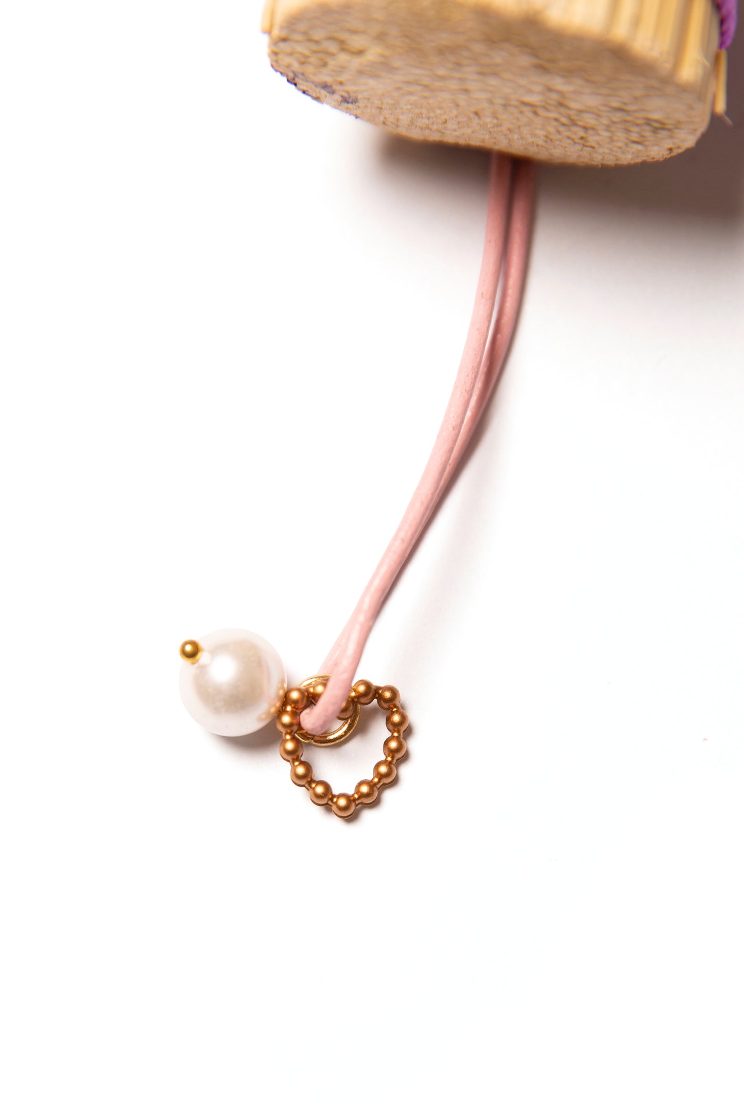 Close up of a leather loop hanger for a handbroom in pink leather with a pearl and gold heart charm against a white background