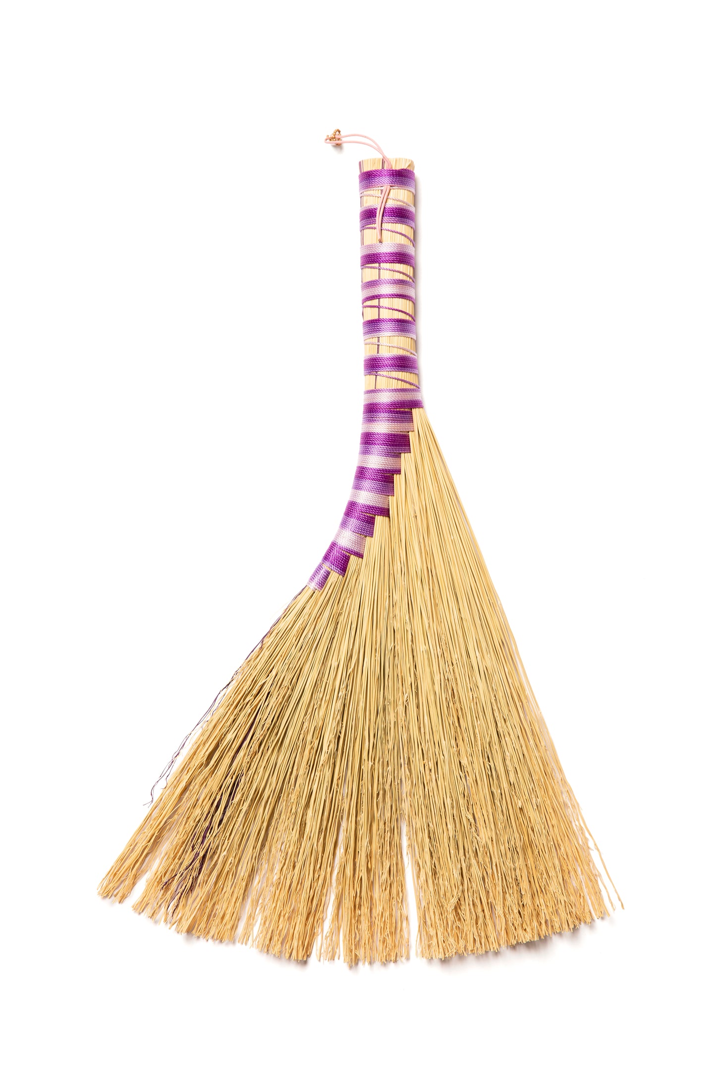 A handbroom with natural broomcorn against a white background made with purple twine.