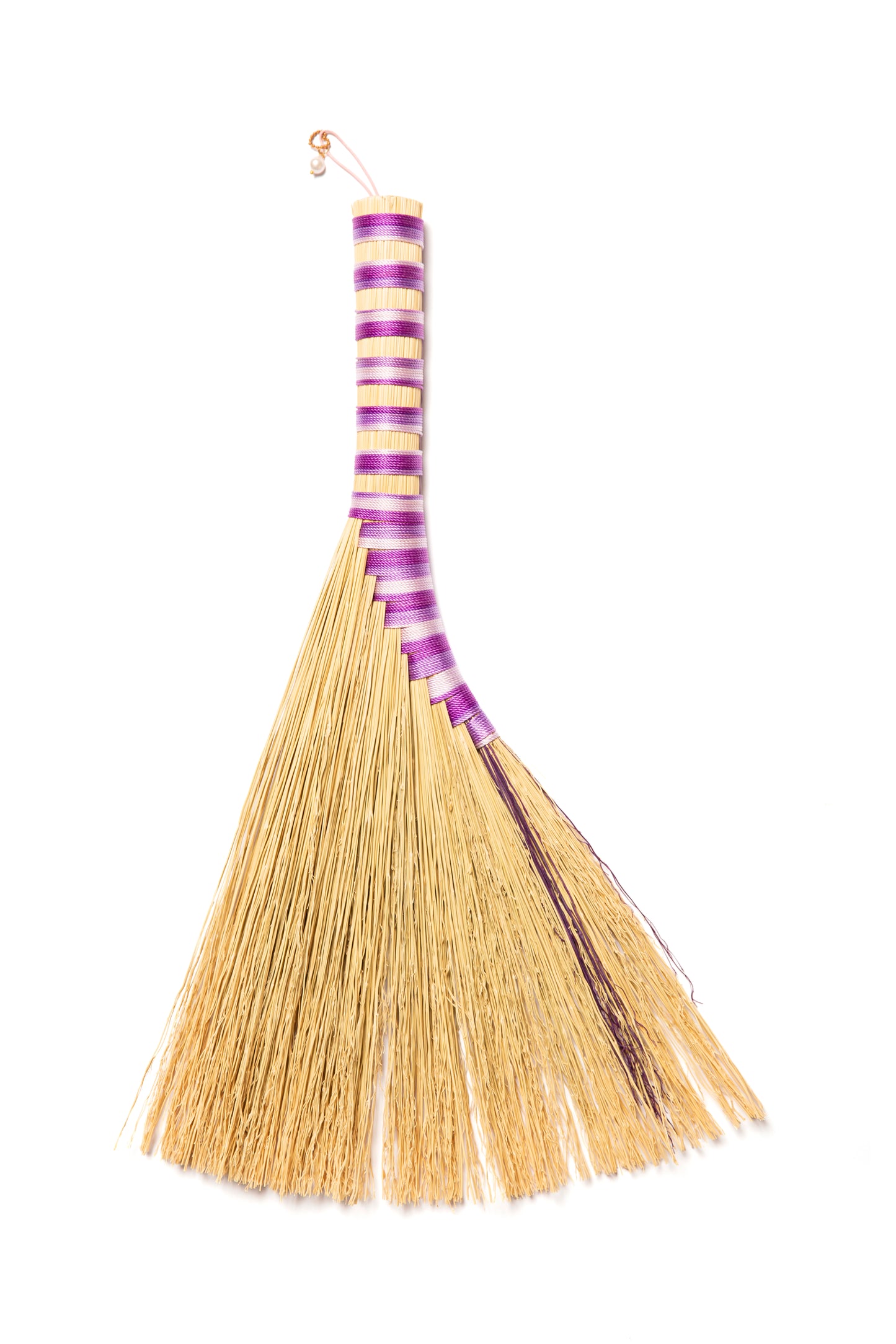A handbroom with natural & purple broomcorn against a white background made with purple twine.