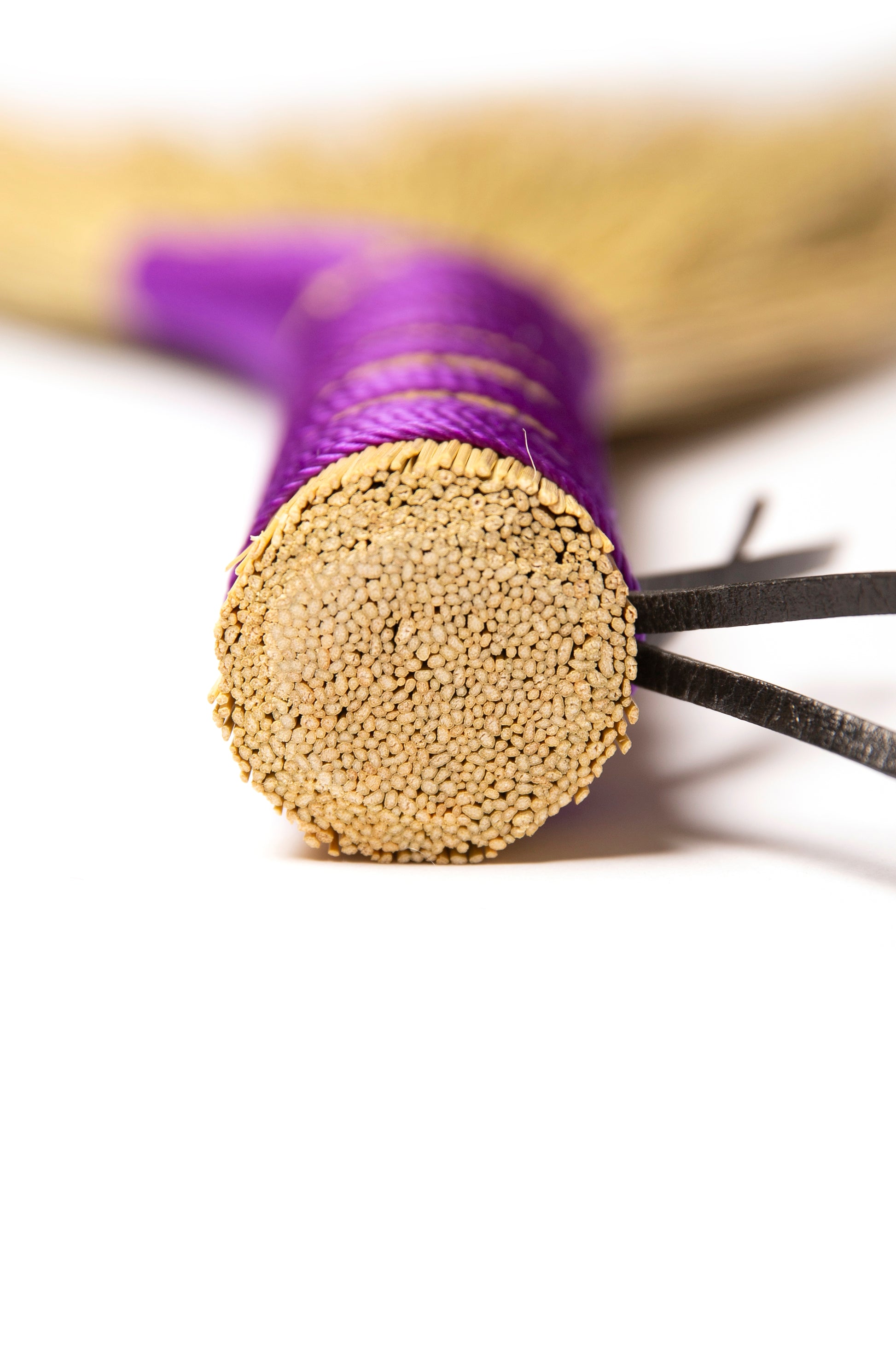 close up of a hand broom handle with purple twine against a white background
