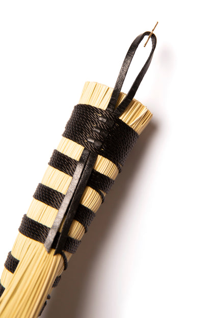 Hand broom handle wound in black twine with natural broomcorn against a white background