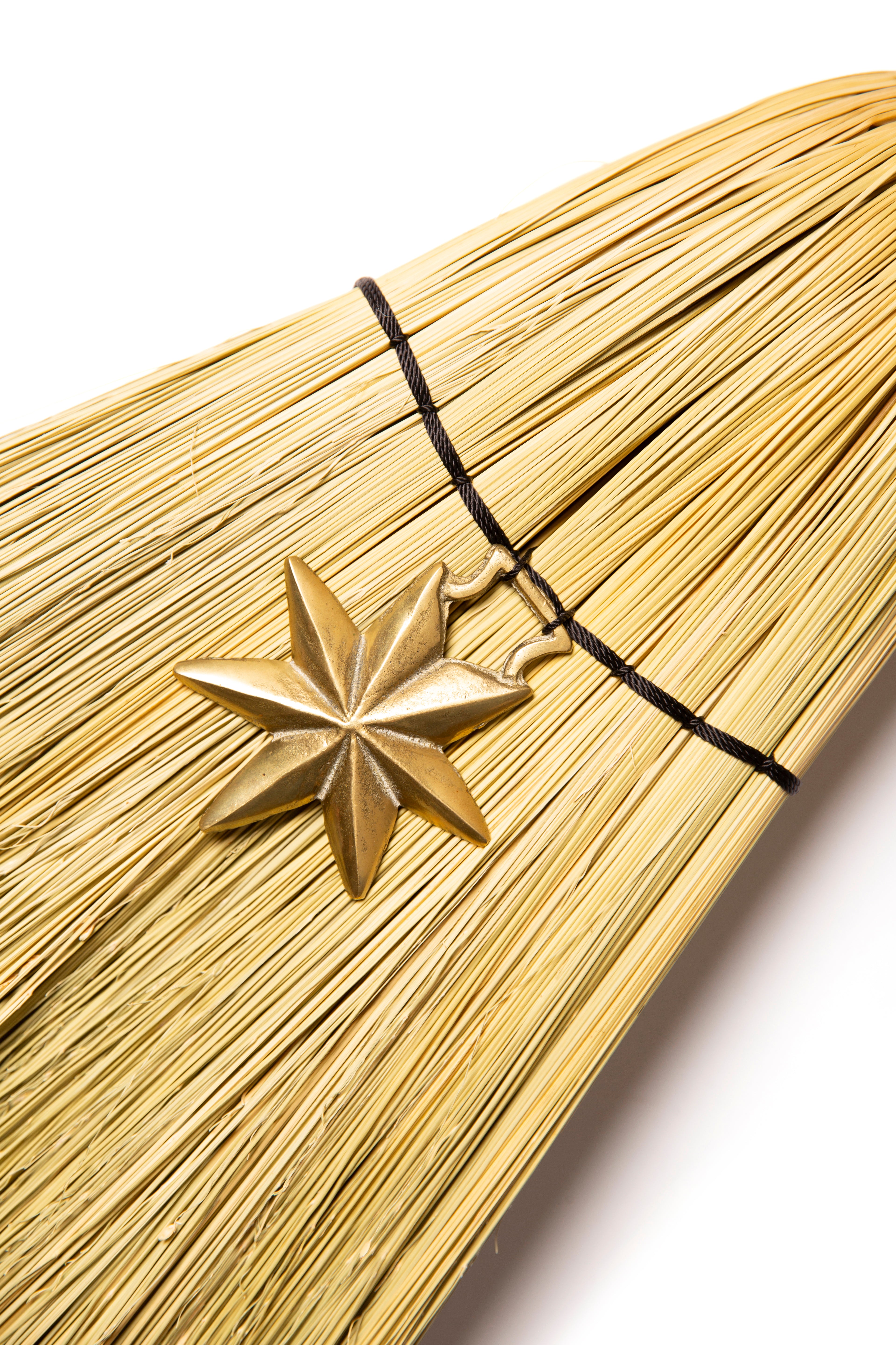 Gold star-shaped pendant on a broom against a white background