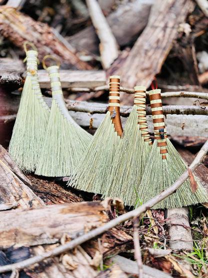 Five hand brooms with crystals and moon pendants attached set amongst a woodpile in the forest